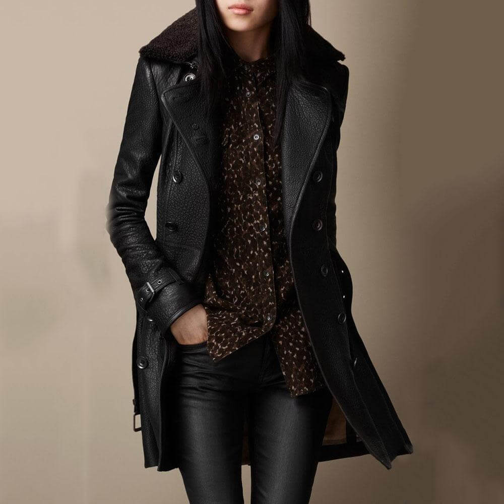 Person wearing a black coat with fur hood and leather gloves on a beige background